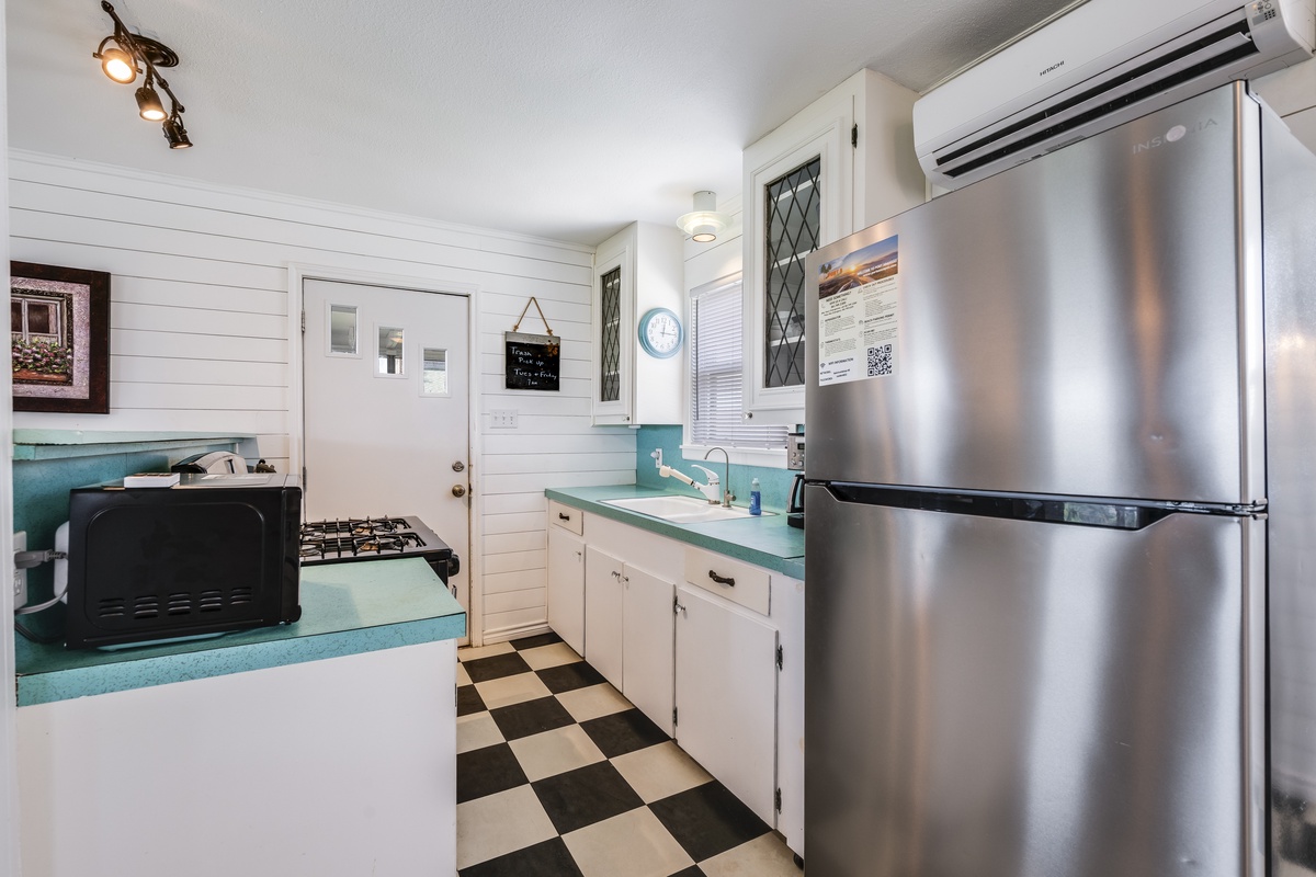 Your charming retro kitchen features everything you need—stainless steel appliances, gas stove, and crisp white cabinetry with turquoise countertops over classic checkered floors.