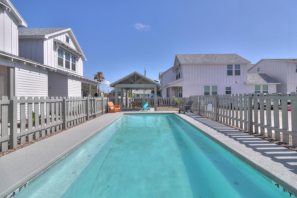 Dive into your private paradise with this stunning turquoise pool surrounded by colorful lounge chairs and charming coastal cottages.