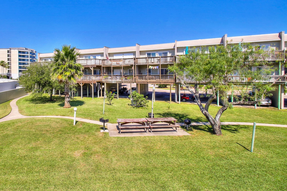 Beachfront property with spacious grounds, mature trees, and convenient parking beneath multi-level balconied buildings.