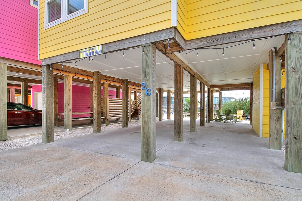 Covered parking beneath colorful beach house with concrete floors and wooden support posts.