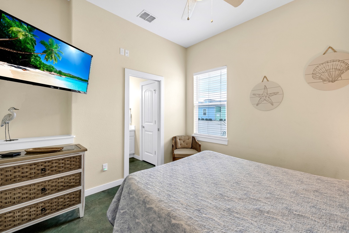 Drift off to coastal dreams in your serene bedroom, featuring a wall-mounted TV and cozy seating nook by the bright window.