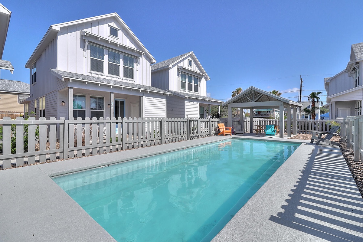 Modern coastal home with private swimming pool and covered outdoor entertaining area under clear blue skies.