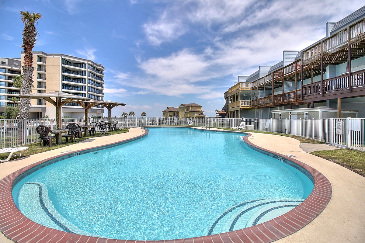 Cool off in this sparkling pool with comfortable seating nearby, all under beautiful blue skies at your beachfront getaway.