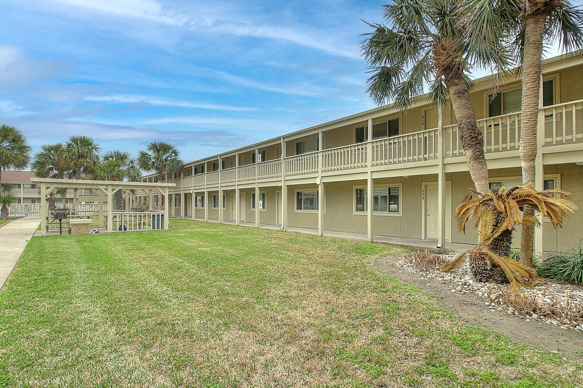 Two-story beachside property featuring tropical landscaping with palm trees and spacious courtyard areas surrounded by balconied accommodations.