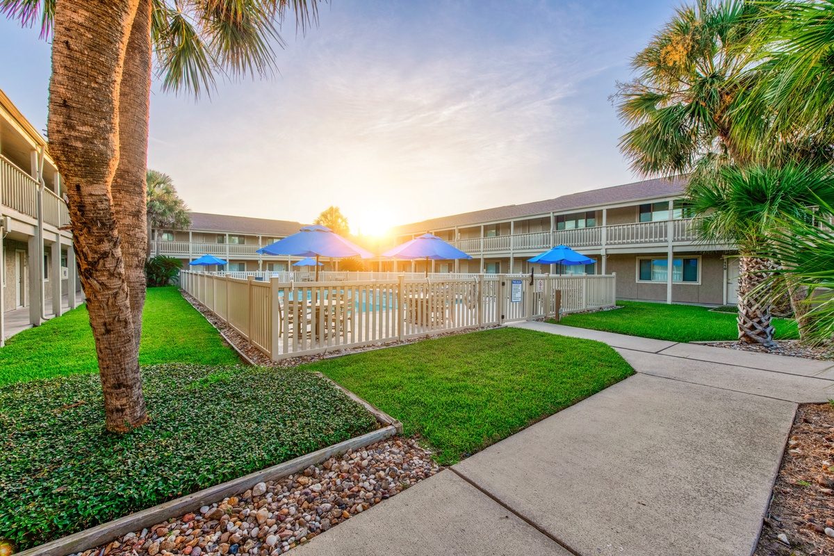Property complex featuring a sparkling pool area surrounded by tropical palm trees at sunset.