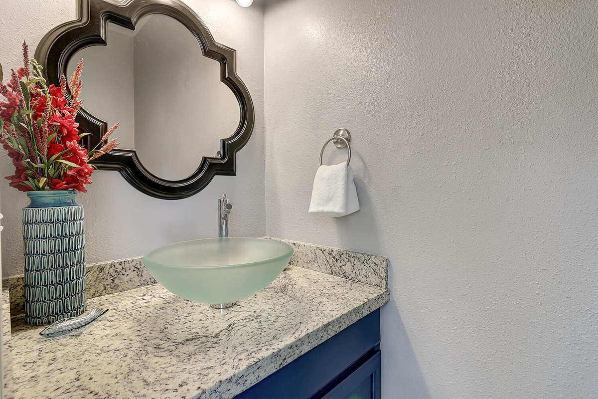 Your elegant powder room features a stunning glass vessel sink atop granite countertops, with thoughtful touches and fresh florals to welcome you.