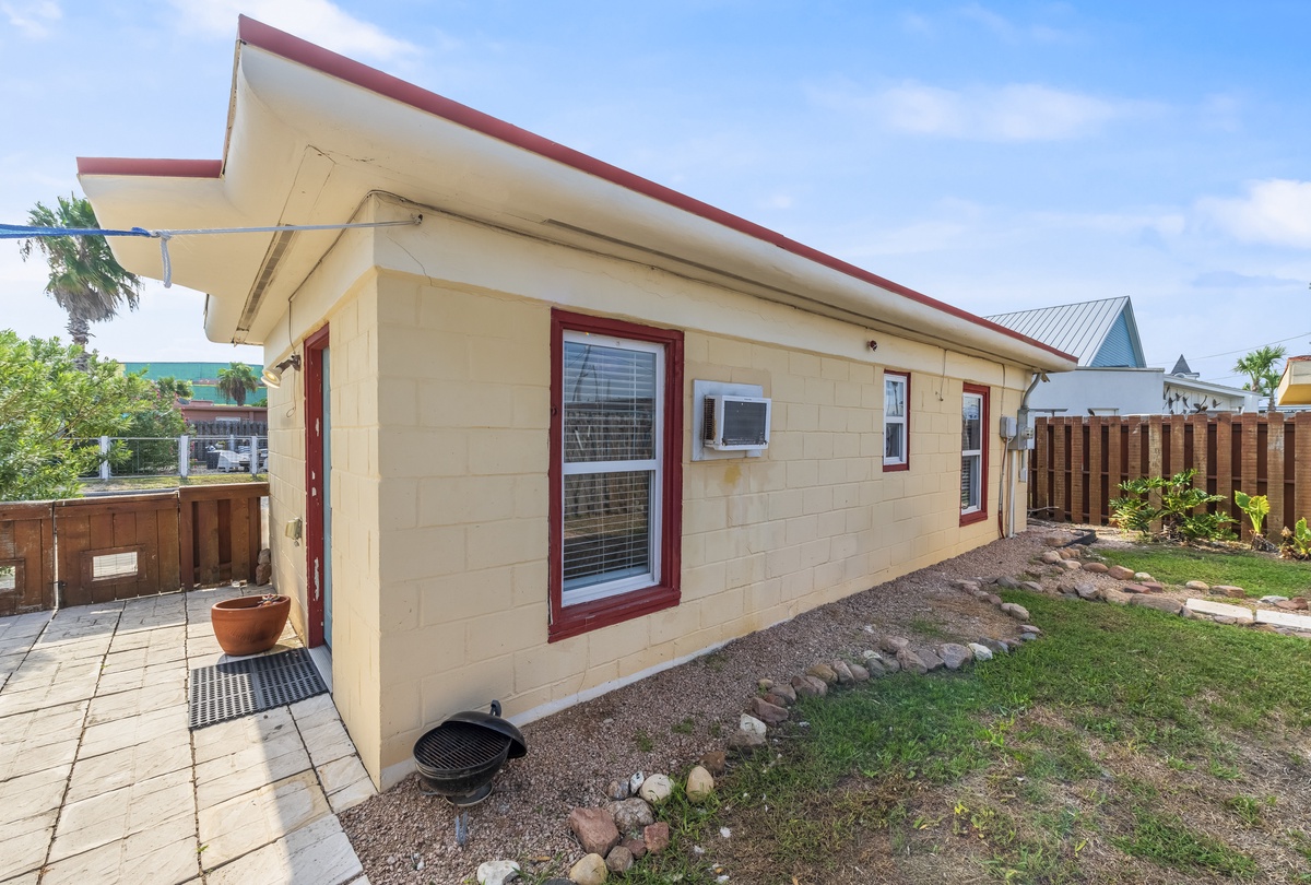 A charming beachside cottage with red trim and private patio, surrounded by tropical landscaping in a peaceful residential setting.