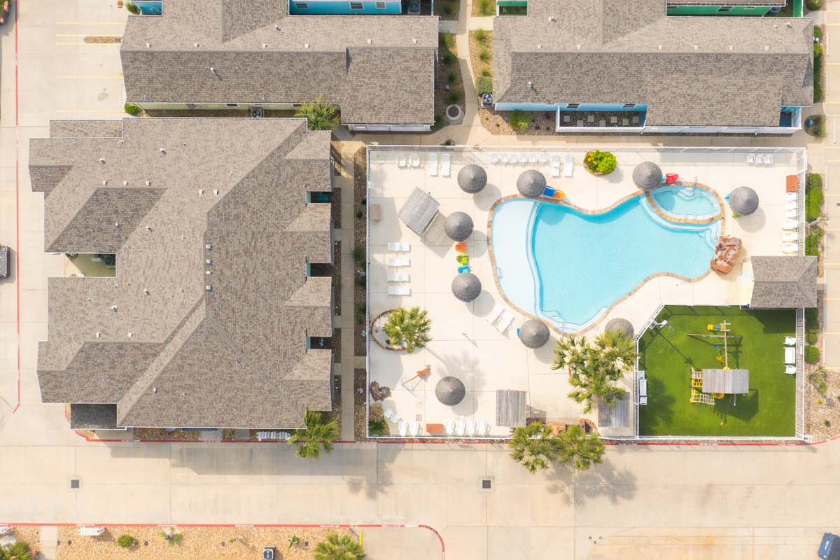 Aerial view showcasing the property's resort-style pool complex with curved design, surrounding deck, and children's play area within the residential community.