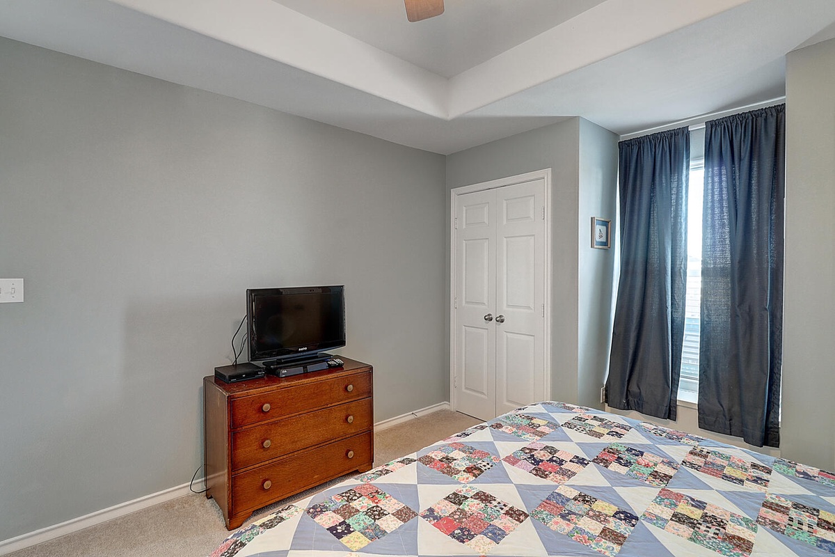 Unwind in your cozy bedroom featuring a comfortable bed, flat-screen TV, and dresser storage beneath elegant coffered ceilings.