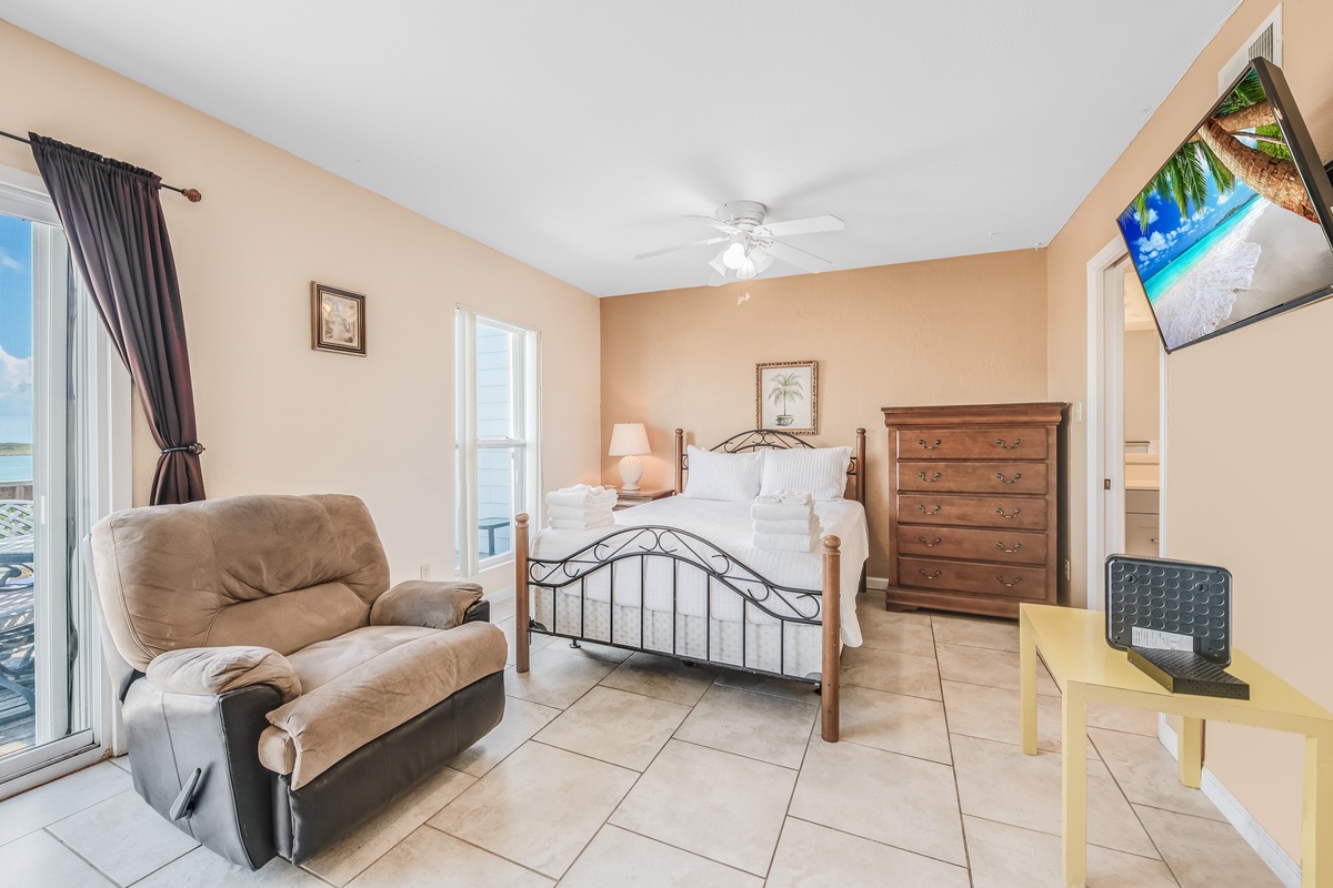 Unwind in your spacious bedroom featuring a comfortable recliner, elegant furnishings, and entertainment system for peaceful relaxation.
