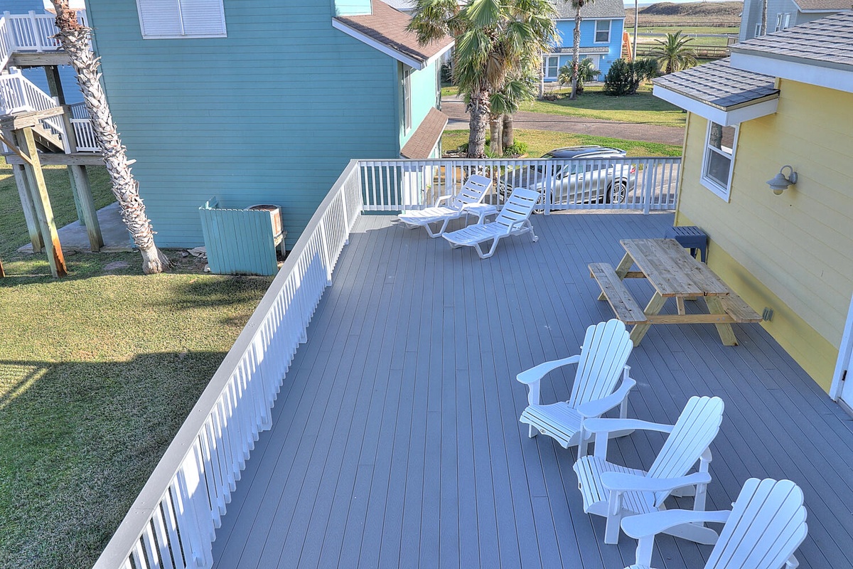 Expansive deck with comfortable seating and dining area overlooking a peaceful coastal neighborhood with colorful beach houses.
