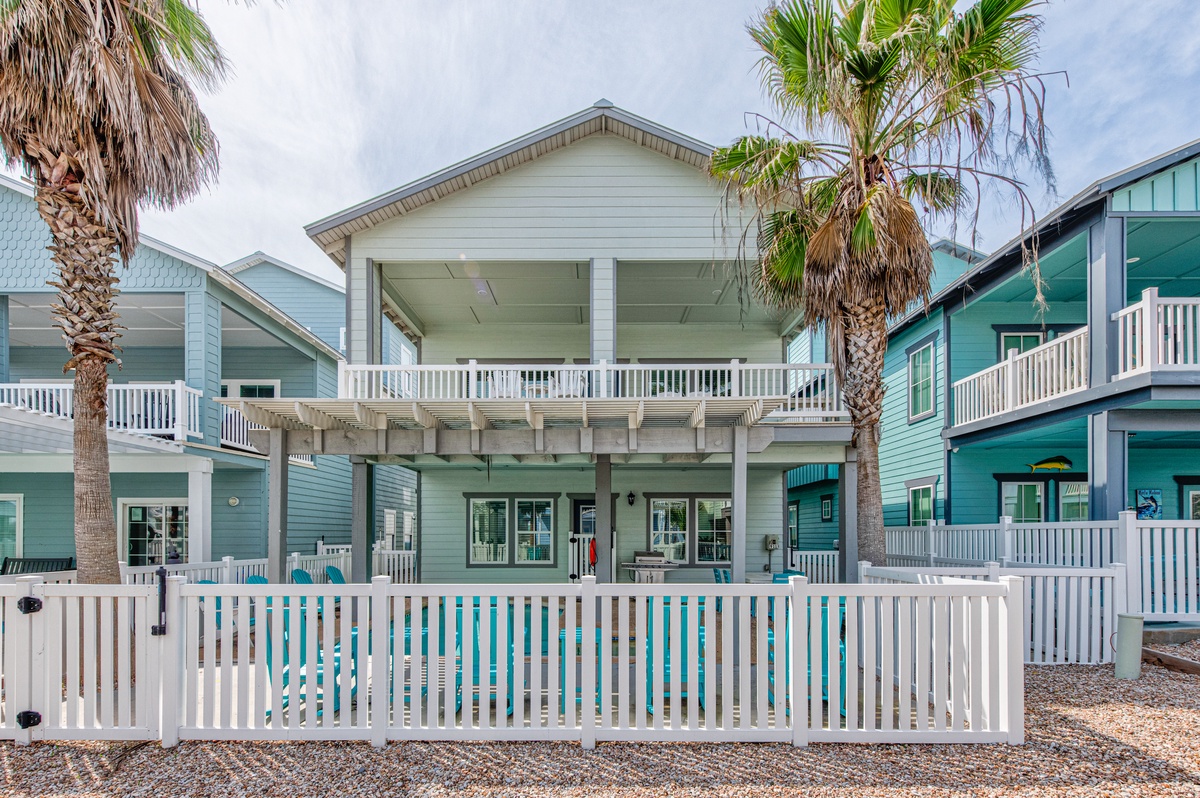 Charming beachside cottage with white picket fence and tropical palms in a colorful coastal neighborhood.