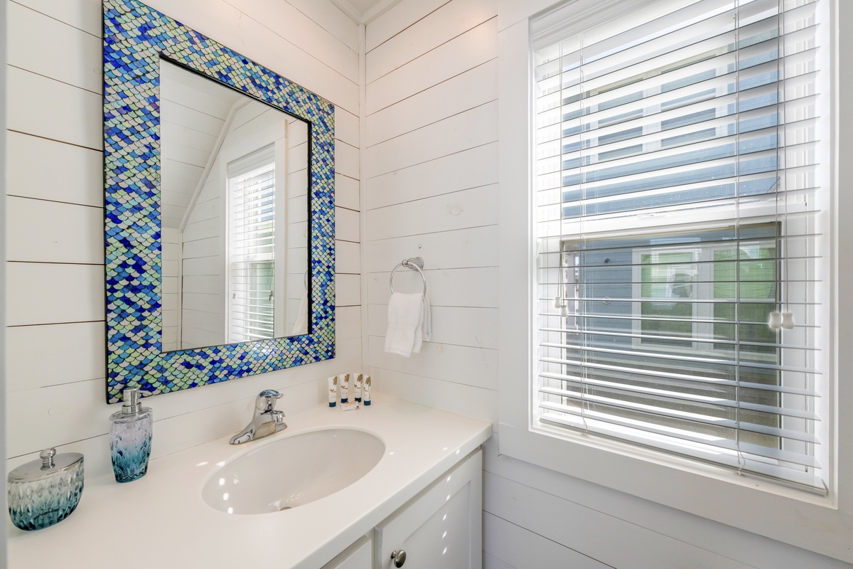 Freshen up in your bright, coastal-inspired bathroom with stunning blue mosaic accents and natural light streaming through window blinds.