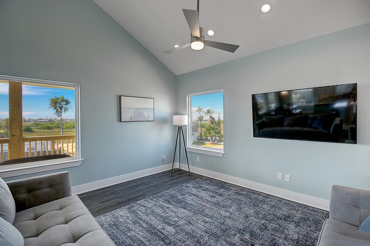 Unwind in your bright living space with comfortable seating, a large TV for entertainment, and stunning windows framing tropical views.