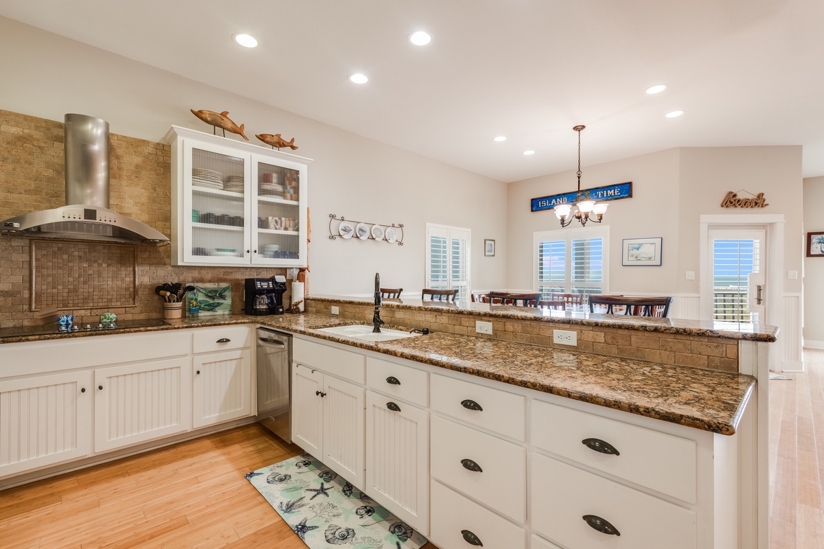 Your fully equipped kitchen features granite countertops, white cabinets, and modern appliances—perfect for preparing meals while enjoying ocean views through the windows.
