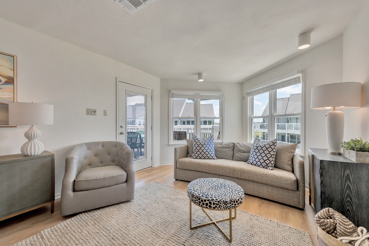 Sink into plush gray seating with stylish pillows while natural light floods your elegant living space through oversized windows.