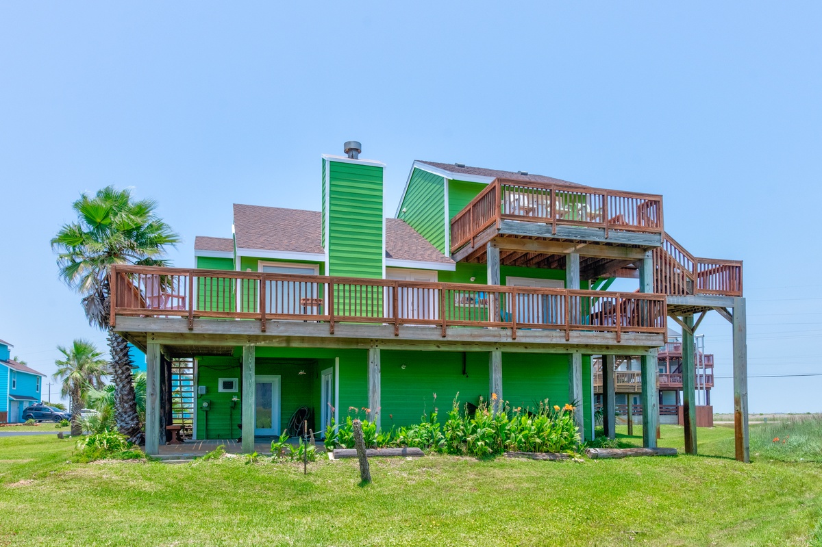 Bright green beach house with expansive wooden decks and tropical landscaping in a coastal neighborhood setting.