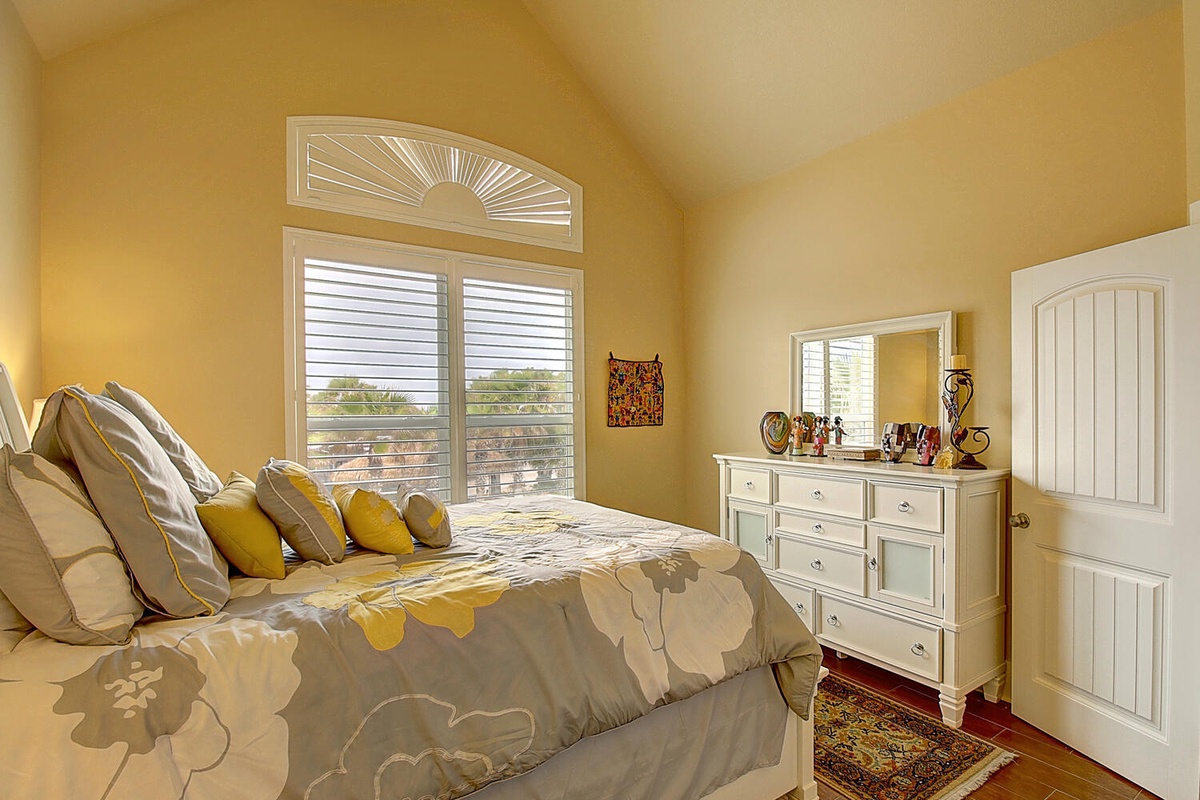 Wake up to sunshine streaming through elegant plantation shutters in this cheerful bedroom with warm yellow walls and cozy floral bedding.