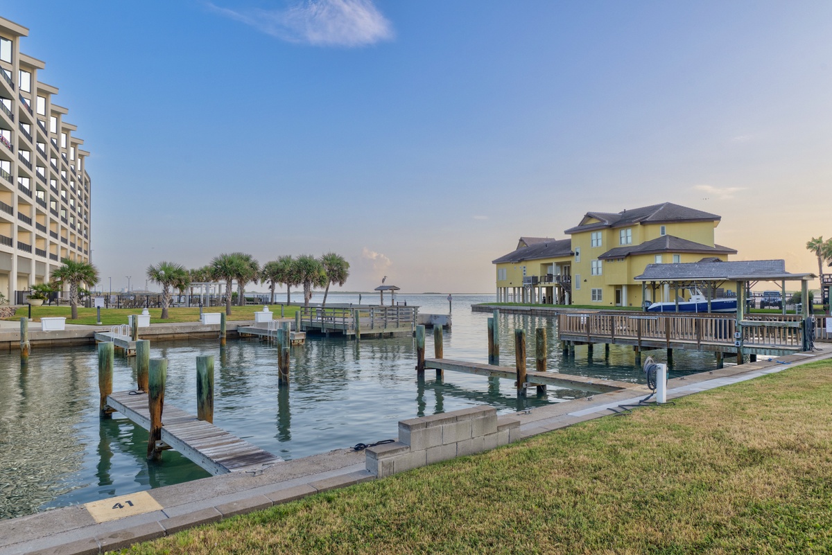 Waterfront property with private boat docks on calm bay waters, flanked by palm-lined lawns and neighboring coastal architecture.