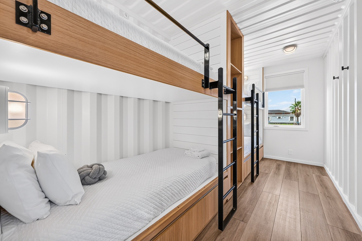 Your custom twin over twin bunk beds rest atop rich hardwood floors, while natural light fills the room and frames a palm tree view through the window.