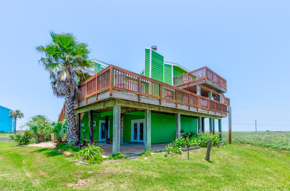 Vibrant green beach house featuring elevated decks and tropical palm trees, set on spacious waterfront grounds.