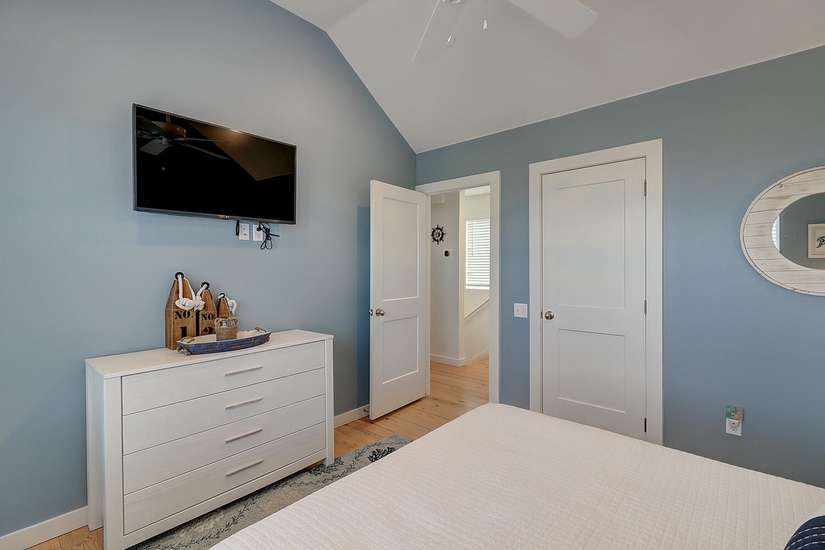 Your calming bedroom features coastal blue walls, a wall-mounted TV for relaxation, and a modern white dresser for your belongings.