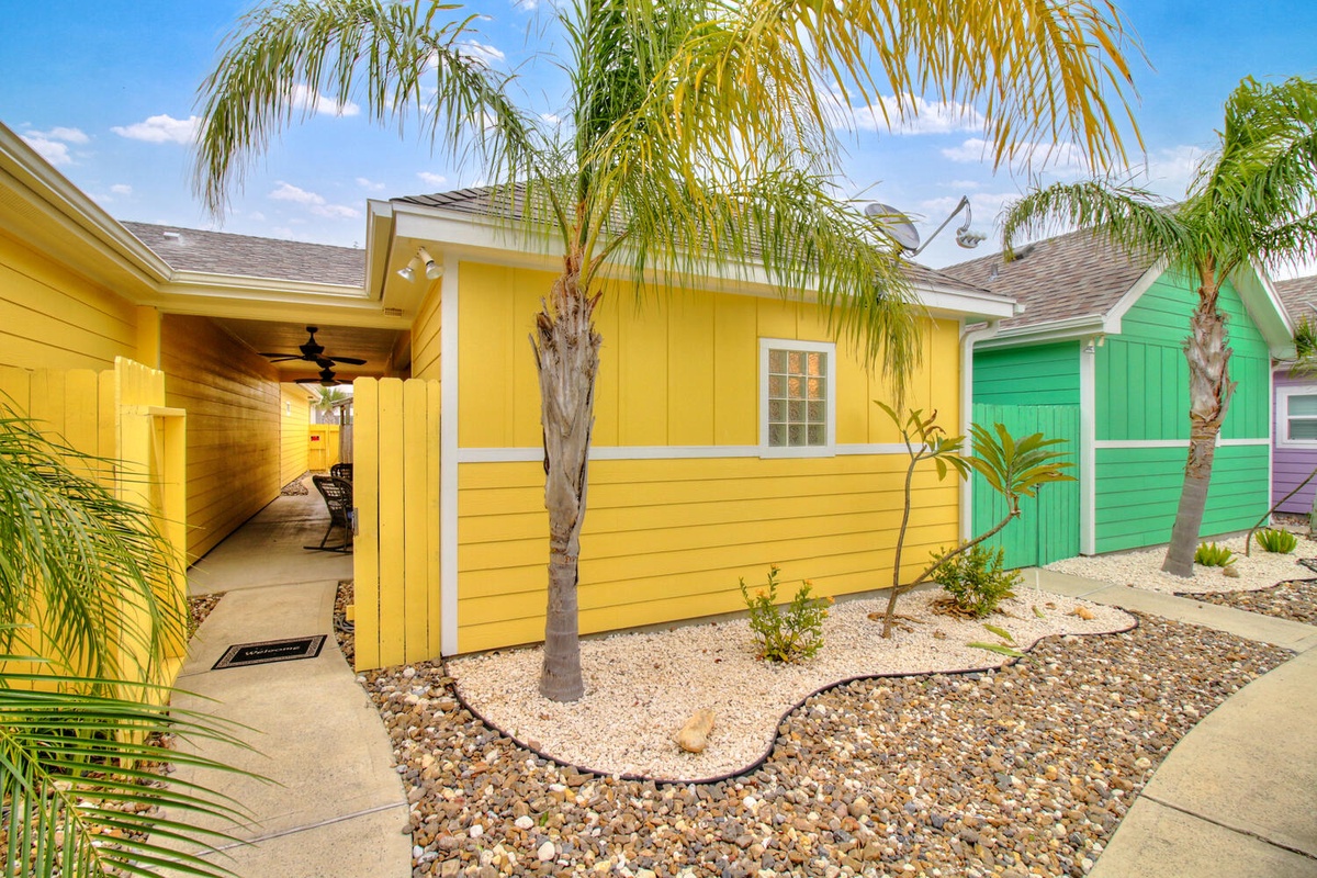Bright yellow and turquoise cottage with tropical palm trees and rock garden landscaping creates a cheerful beach house atmosphere.