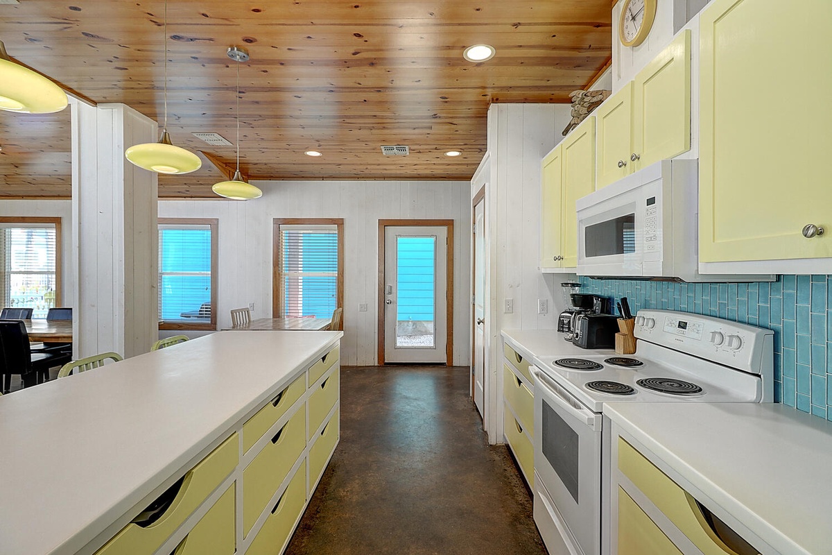 Your bright galley kitchen features cheerful yellow cabinets and turquoise backsplash, perfect for preparing coastal meals with ocean views.