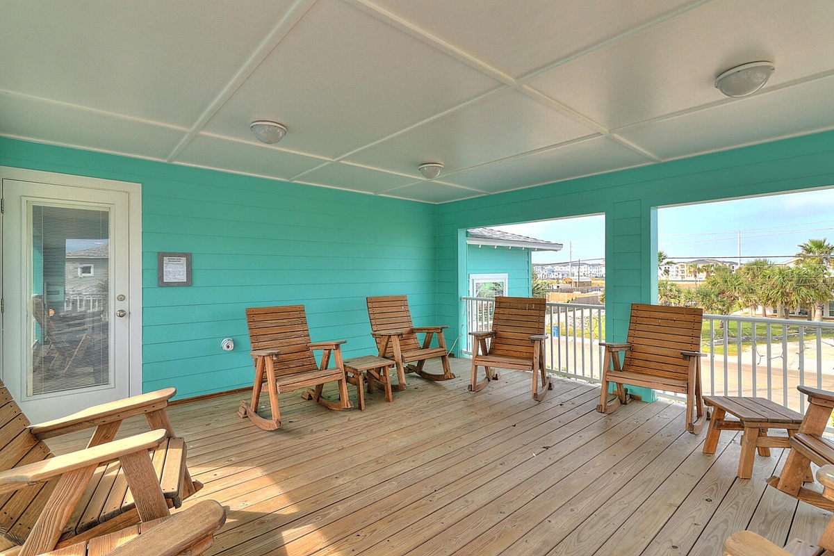 Relax in your covered deck with wooden rockers and coastal views. The vibrant turquoise walls create a cheerful backdrop for peaceful moments.