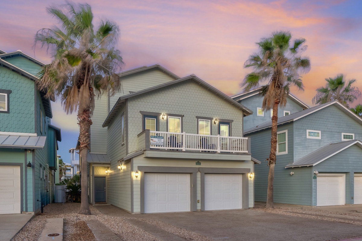 Coastal vacation home featuring a beautiful sunset backdrop with tropical palm trees and convenient ground-level parking in a charming neighborhood setting.