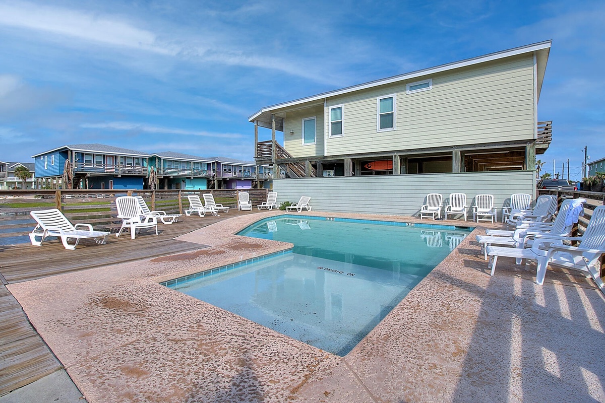 Coastal vacation homes with a refreshing swimming pool surrounded by comfortable lounge chairs under bright blue skies.