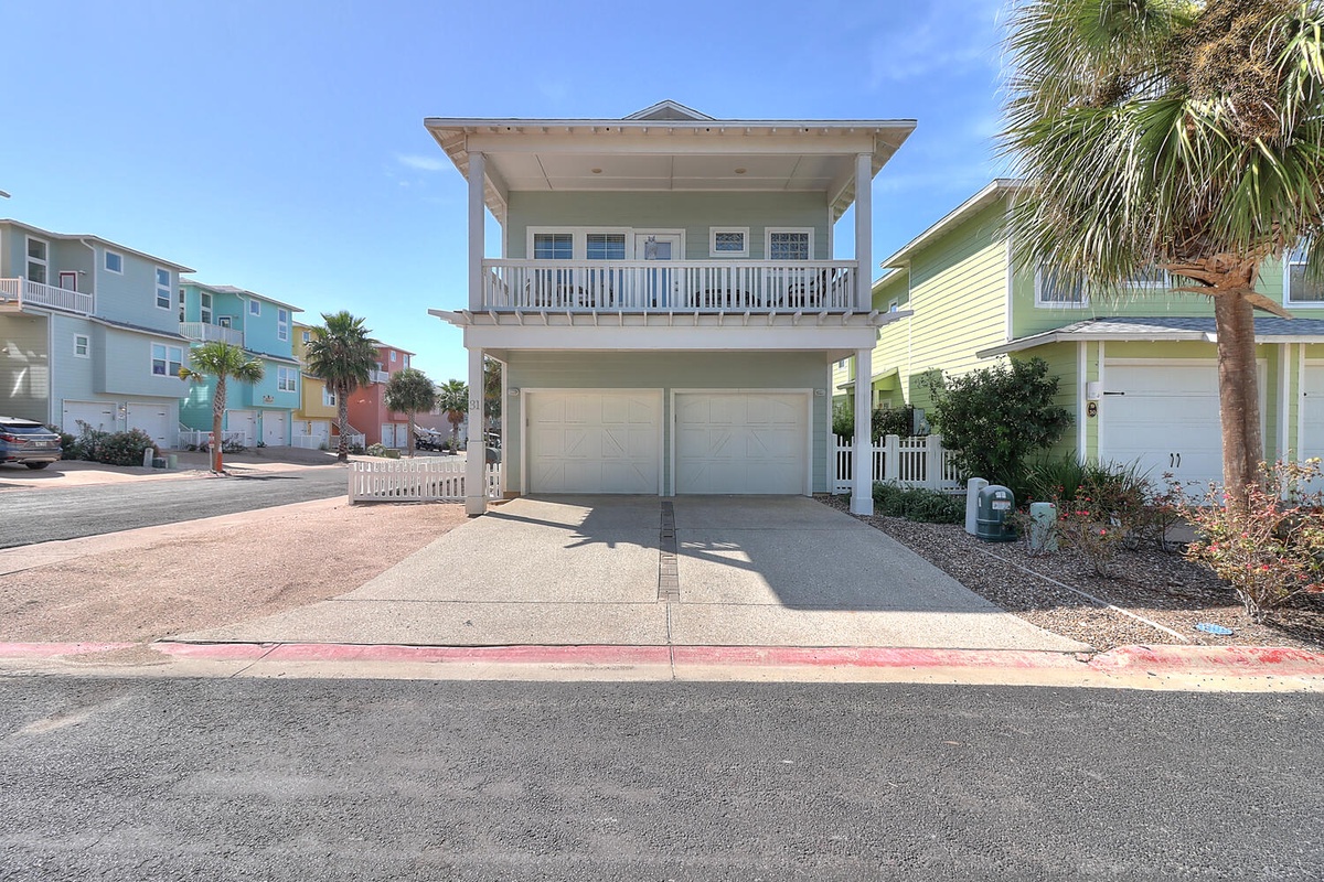 Charming coastal rental home with spacious two-car garage and covered balcony, nestled among colorful beach houses in a peaceful neighborhood.