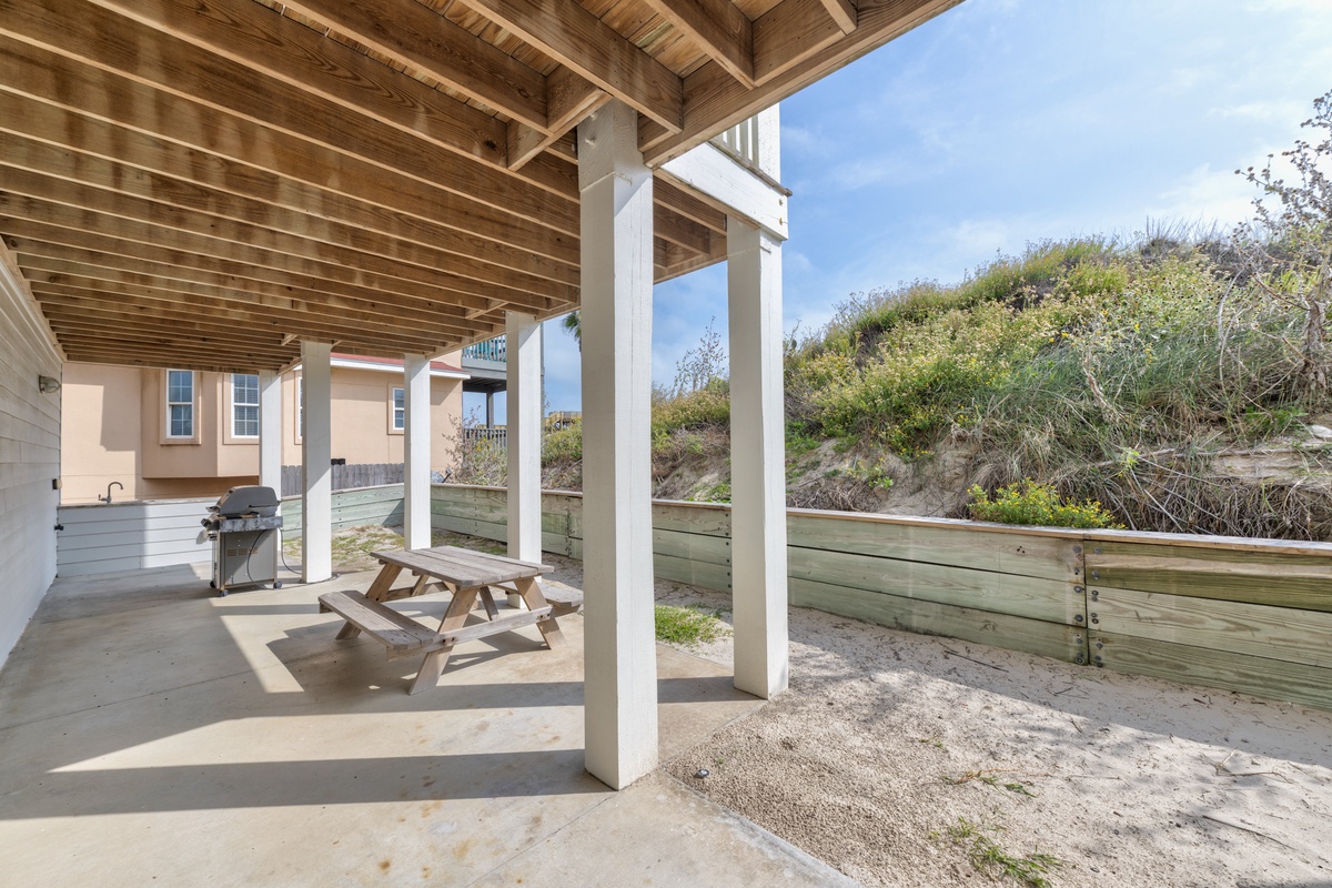 Your covered patio offers the perfect spot for outdoor dining with a picnic table and BBQ grill, all surrounded by natural dune vegetation.