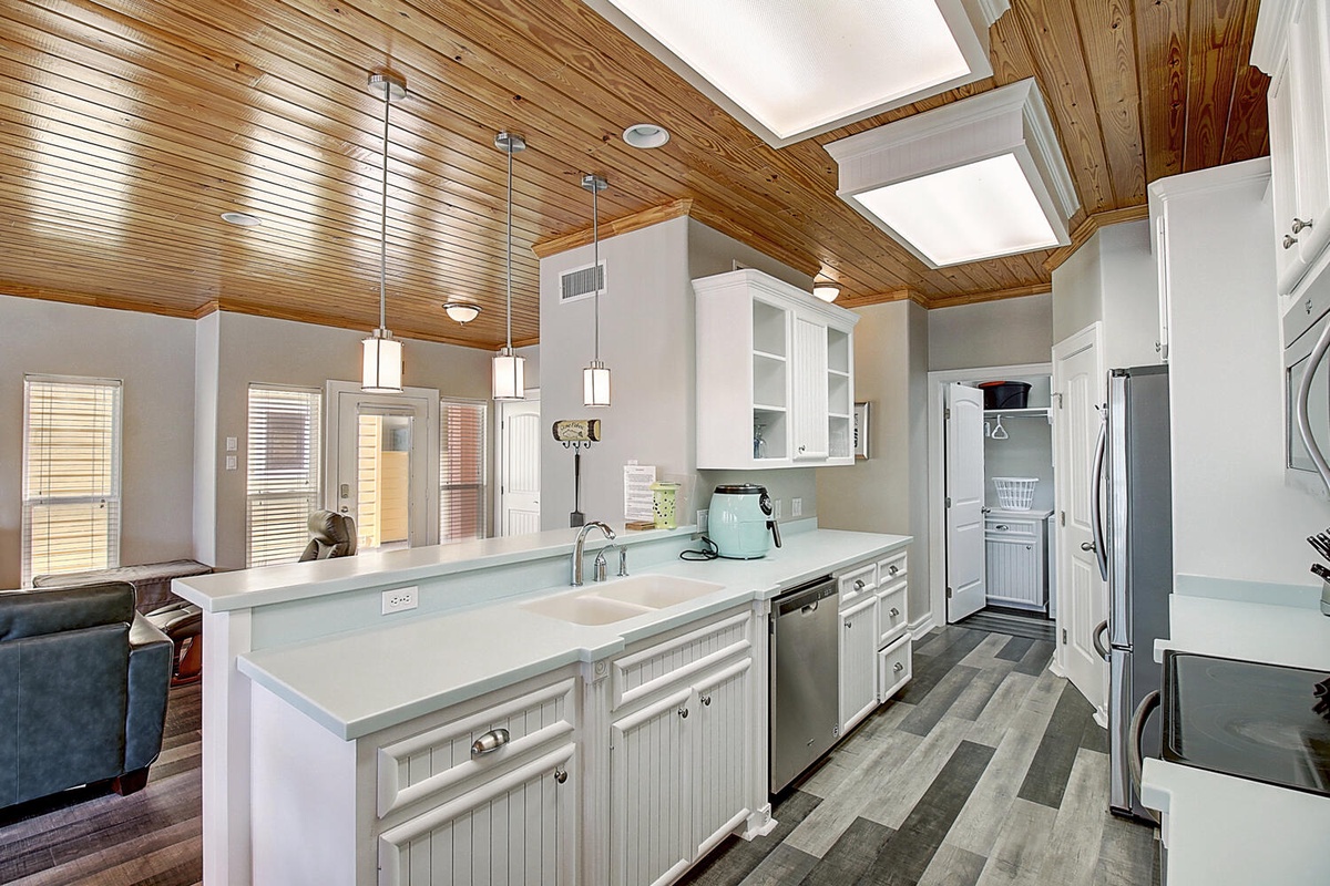 You'll love preparing meals in this bright, open kitchen featuring white cabinetry, pendant lighting, and warm wood ceiling details.