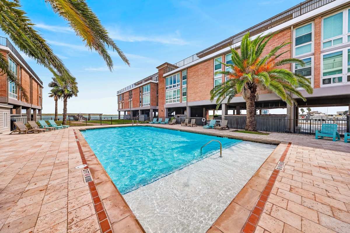 Sparkling pool framed by palm trees with water views beyond the property building—an inviting spot to relax under sunny skies.