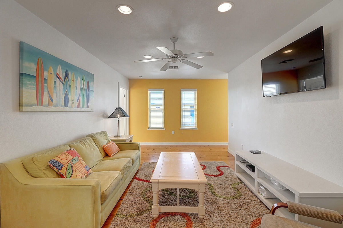 Relax in your bright living room with sunny yellow accent wall, comfortable sofa, and entertainment center for perfect vacation evenings.