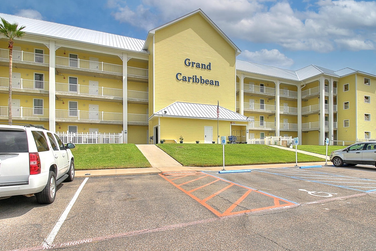 The Grand Caribbean resort features bright yellow buildings with multiple balconied floors and convenient parking areas for guest arrivals.