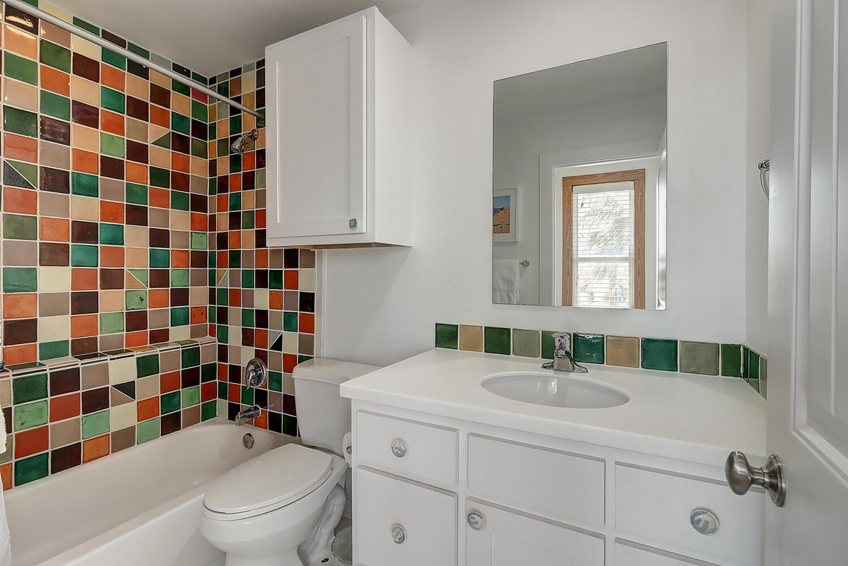 Refresh in your vibrant bathroom featuring colorful mosaic tiles, bright white vanity, and bathtub-shower combo for your daily rituals.