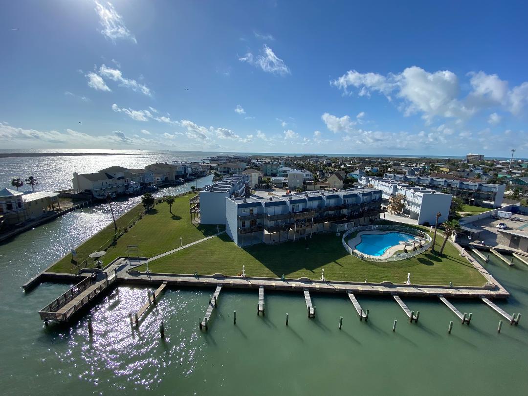 Aerial view of waterfront resort featuring marina docks, swimming pool, and scenic coastal community setting.