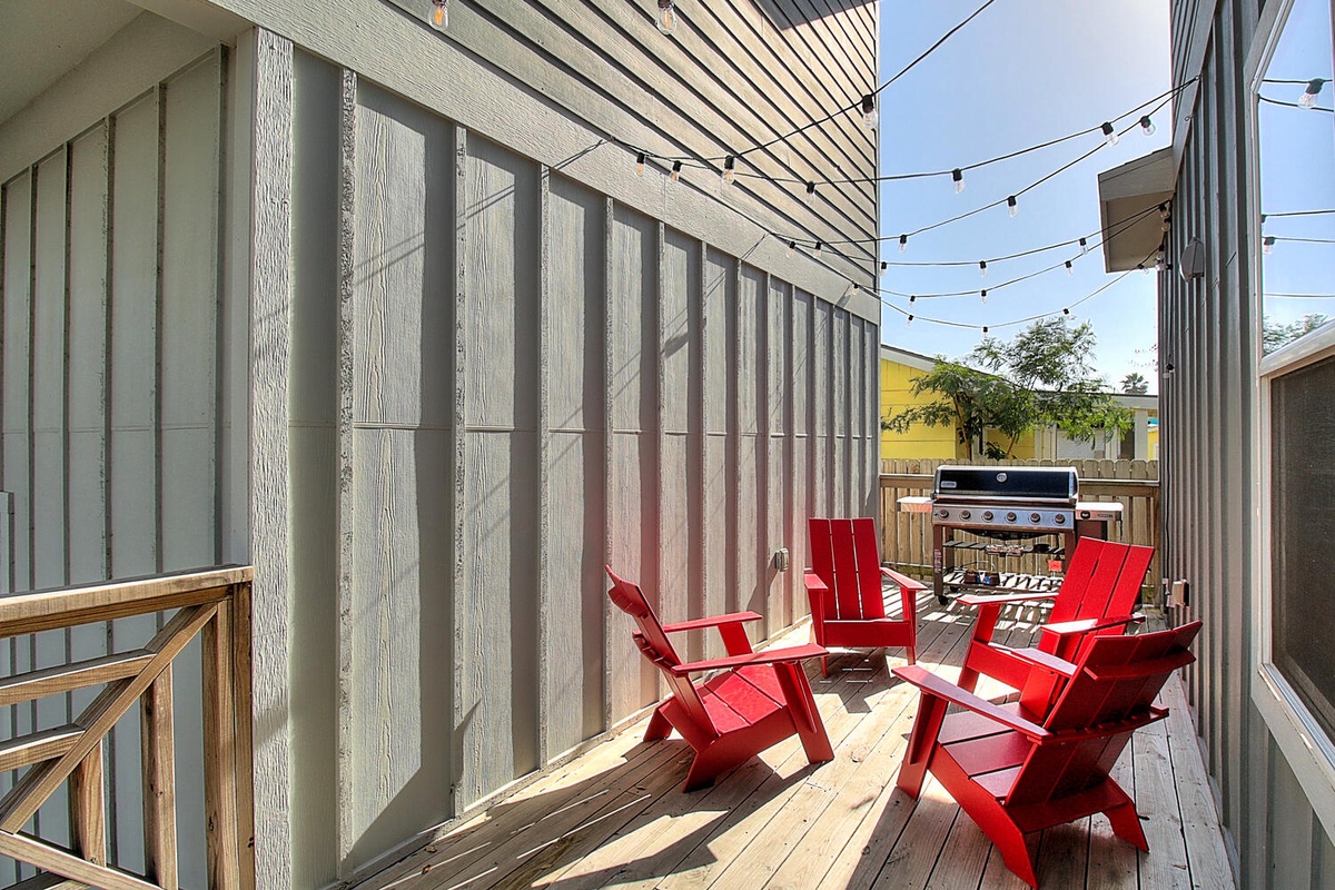 Your private deck awaits with bright red chairs and BBQ grill, perfect for sunny morning coffee or evening grilling sessions.