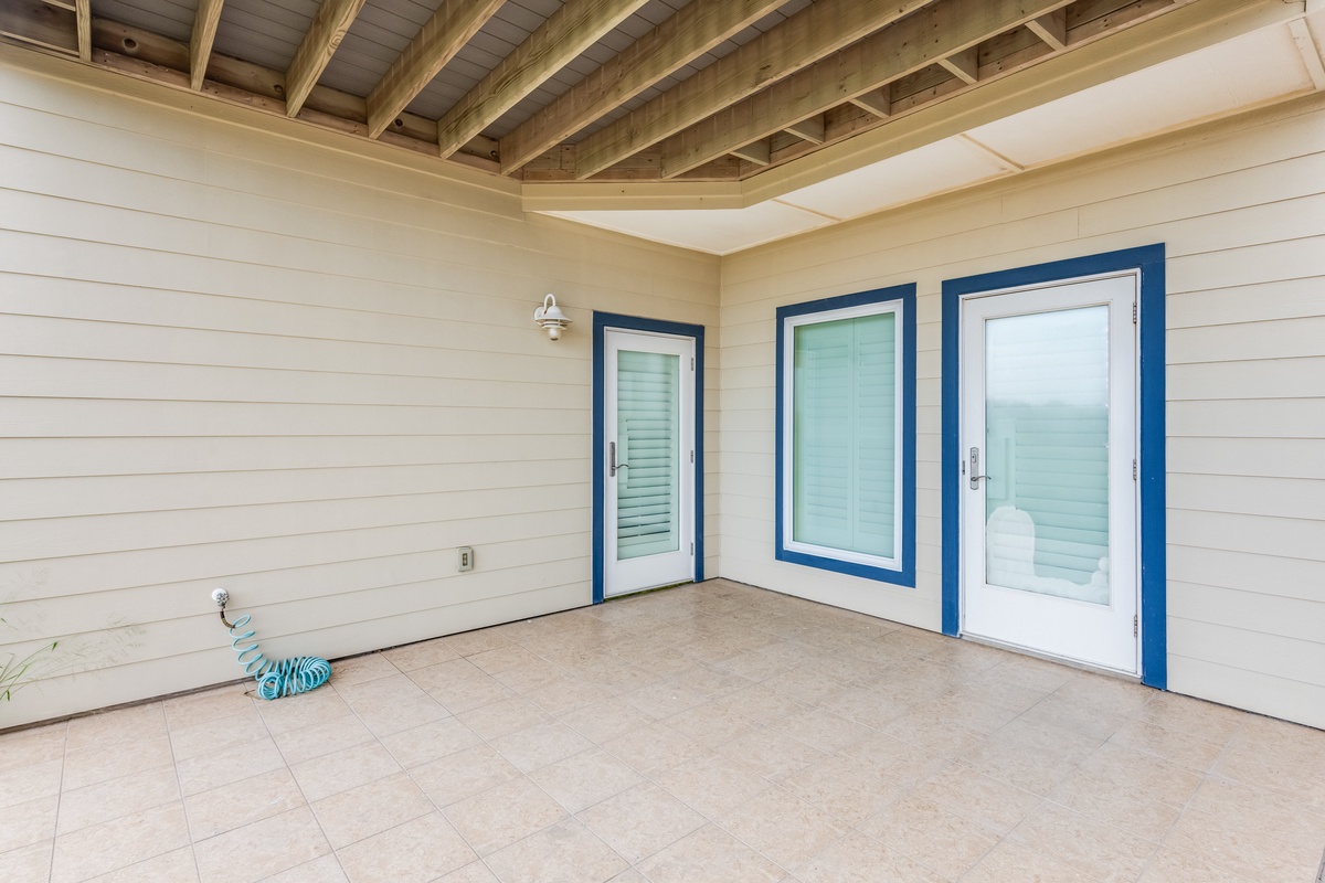Your private covered patio offers a peaceful retreat with rustic beams overhead and ocean views through bright blue-framed doors.