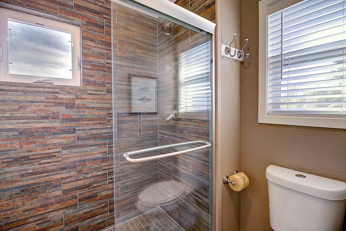 Step into your private sanctuary with a stunning stone-tiled shower featuring glass doors and built-in seating for ultimate comfort.
