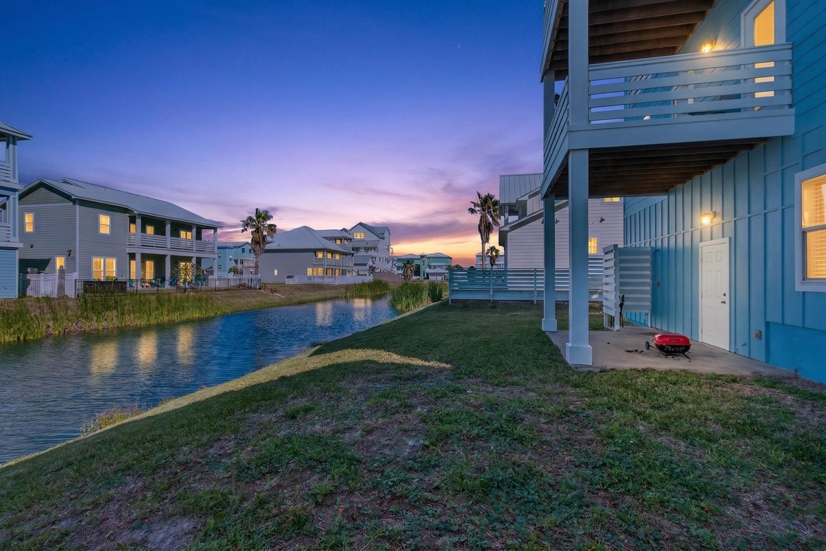 Beautiful coastal neighborhood with modern beach houses along a tranquil waterway, featuring stunning sunset skies and peaceful residential setting.