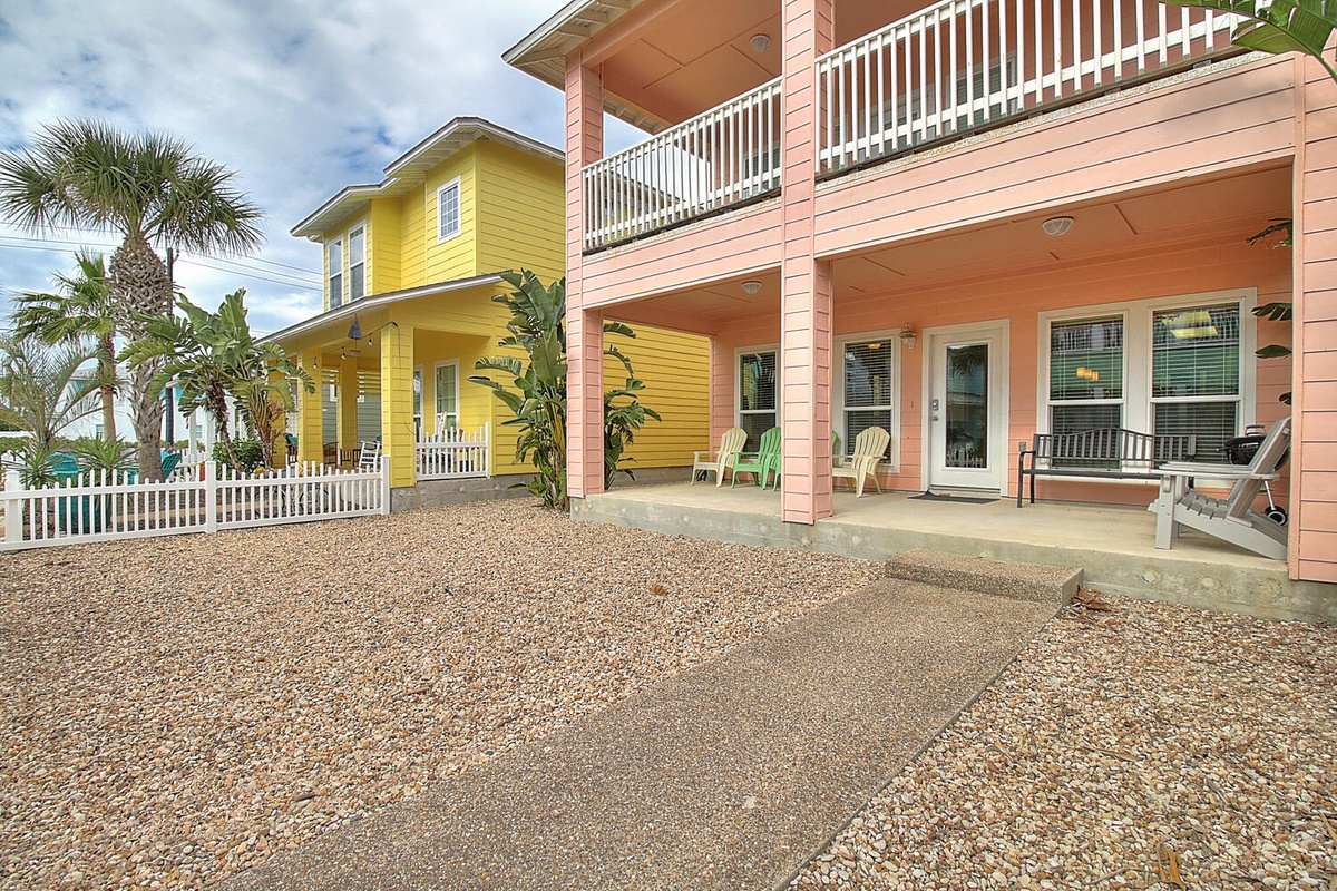 Tropical beach house exterior with colorful coral and yellow buildings, palm trees, and gravel courtyard for a coastal getaway experience.