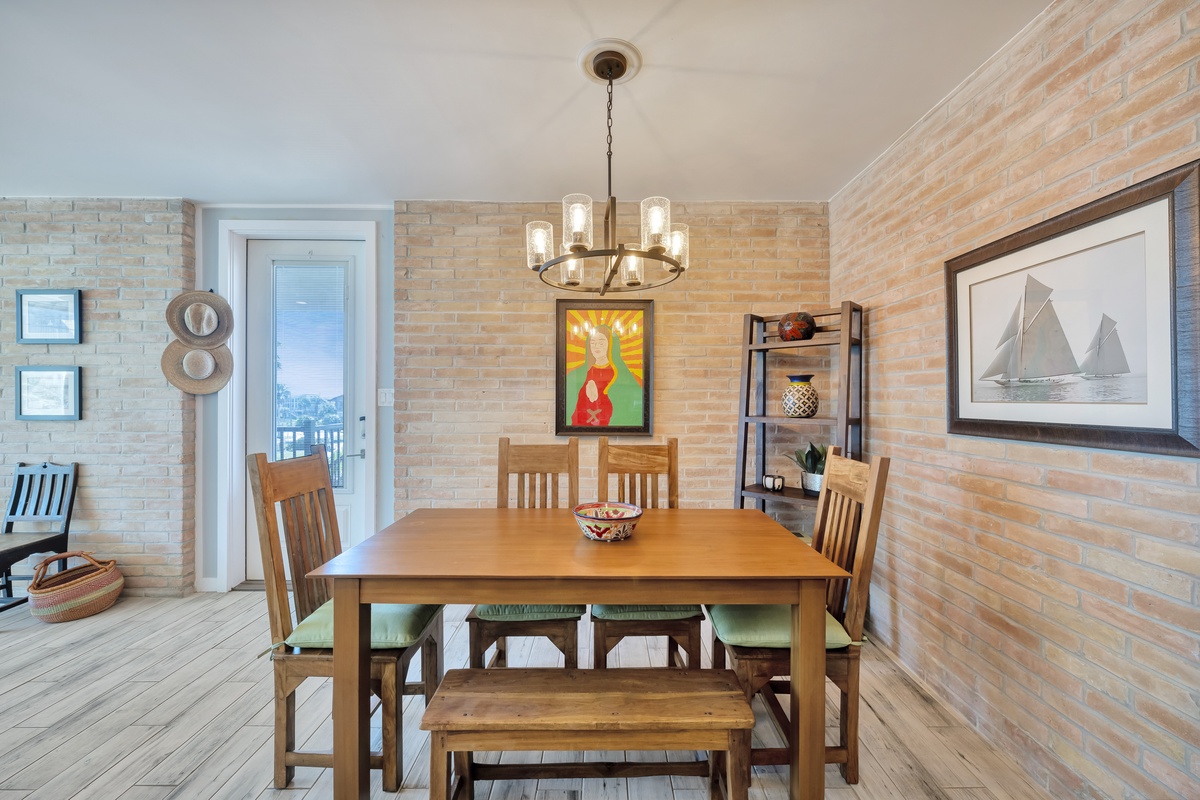 Gather around your inviting dining table where warm brick walls and coastal artwork create the perfect atmosphere for memorable meals together.
