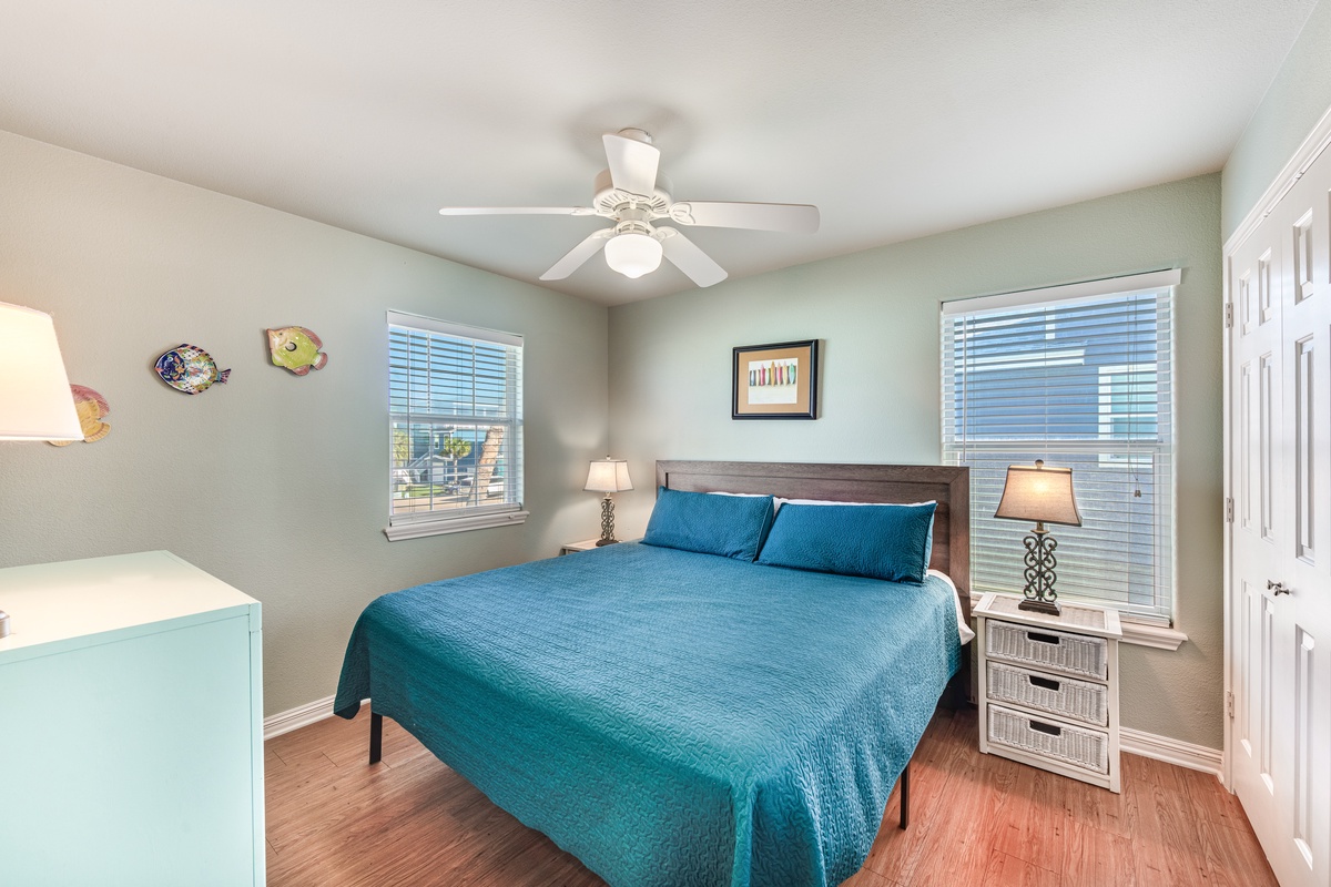 Drift off in your serene bedroom featuring a plush queen bed, soothing coastal colors, and gentle ceiling fan for perfect comfort.