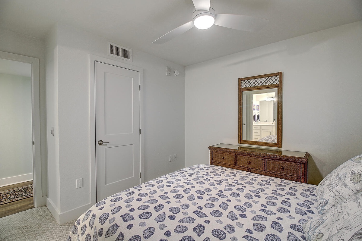 Relax in your serene bedroom featuring coastal-patterned bedding, rattan furniture, and modern comforts like air conditioning and ceiling fan for perfect temperature control.