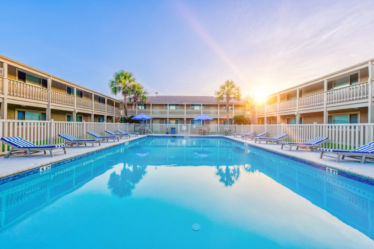 Beautiful resort courtyard featuring crystal-clear pool surrounded by palm trees and comfortable loungers under stunning sunset skies.