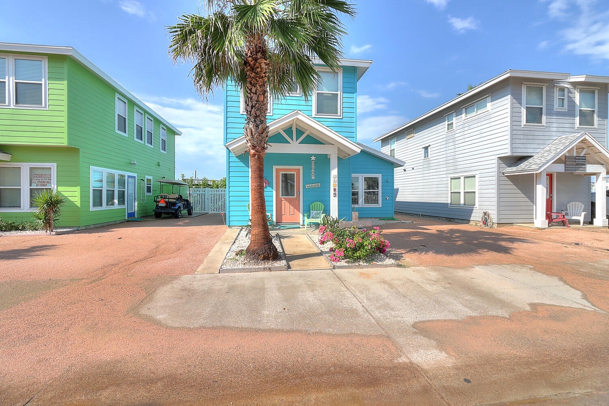 Colorful coastal cottage community with charming turquoise beach house featuring tropical palm tree and vibrant landscaping.
