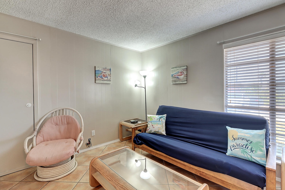 Unwind in your cozy living space with comfy seating, natural light filtering through blinds, and coastal touches that set a peaceful tone.